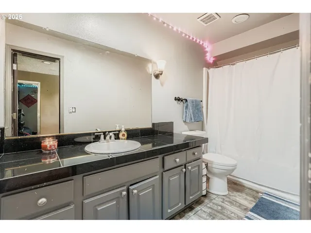 a bathroom with a granite countertop sink a toilet a mirror and shower