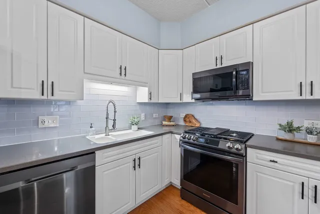 a kitchen with stainless steel appliances granite countertop white cabinets a sink a stove a window and white cabinets