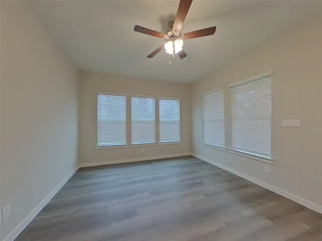 an empty room with wooden floor fan and windows