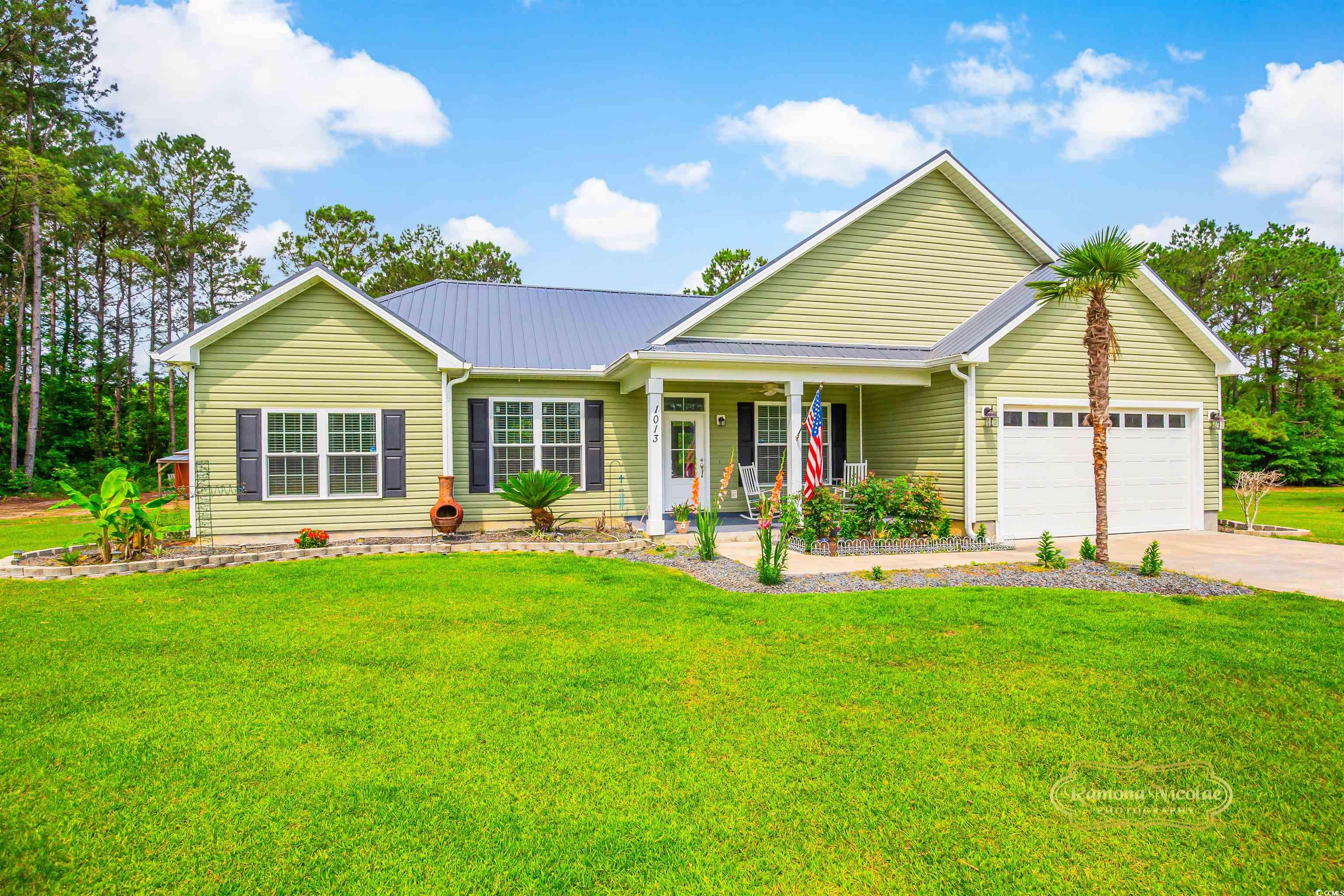 View of front of home featuring an attached garage, a porch, concrete driveway, a front yard, and metal roof