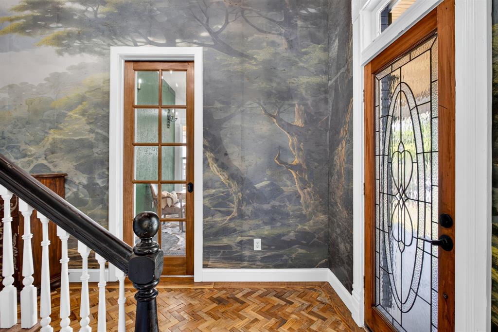 702 West Spring Street Weatherford, TX 76086 - Photo 5 of 39 Herringbone wood flooring entry featuring a rich wood-framed glass door with decorative ironwork, detailed wall mural, and a traditional staircase with white balusters and a dark wood handrail