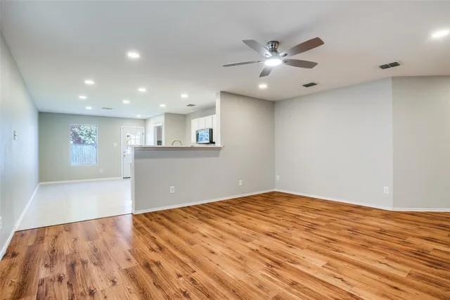 a view of an empty room with wooden floor and a ceiling fan