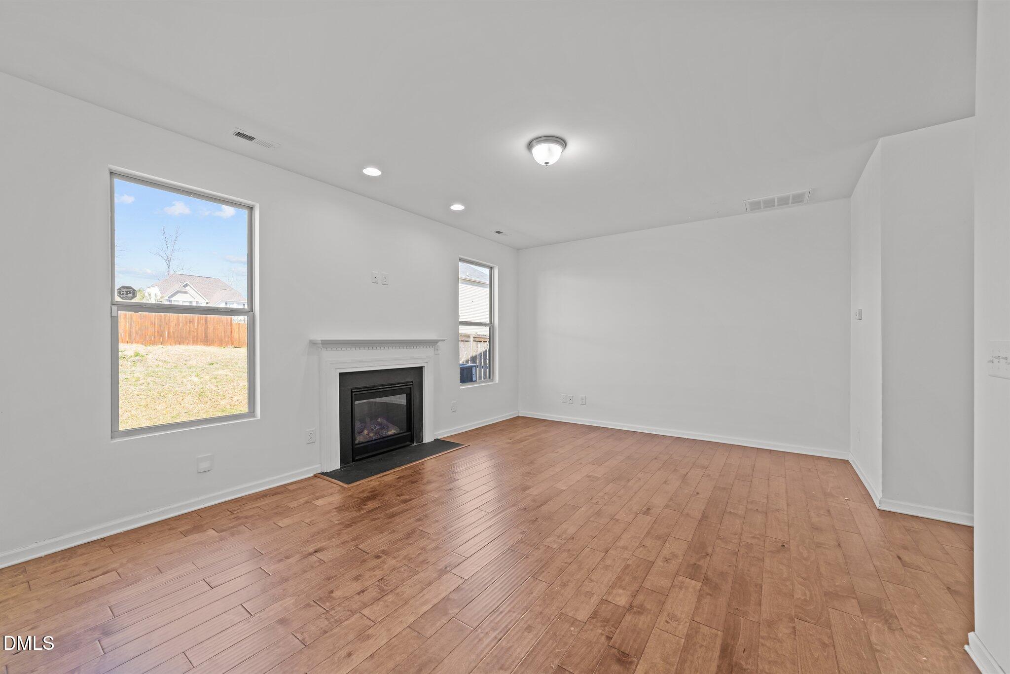 1445 Lombar Street Raleigh, NC 27610 - Photo 4 of 20 an empty room with windows a fireplace and wooden floor