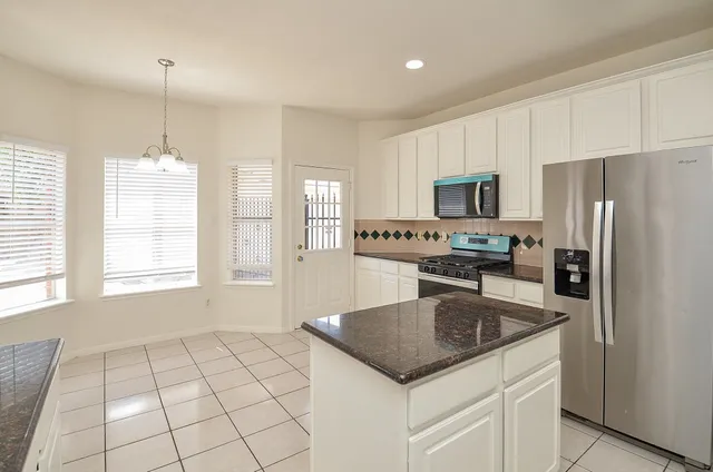 a kitchen with granite countertop a stove a sink a microwave a refrigerator and white cabinets