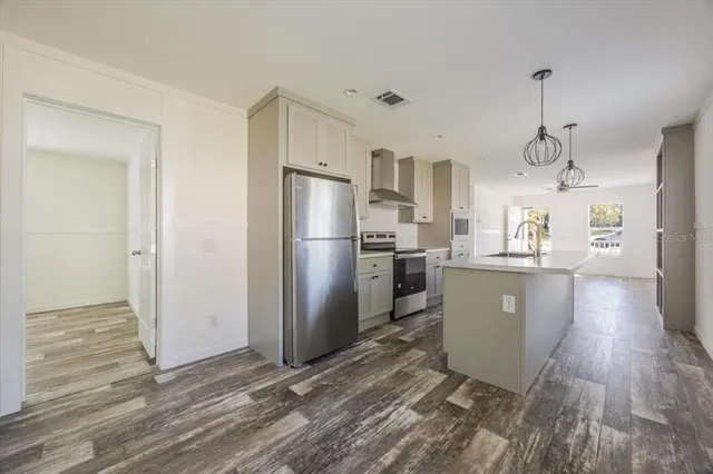 a kitchen with granite countertop a refrigerator a sink dishwasher a stove and white cabinets with wooden floor