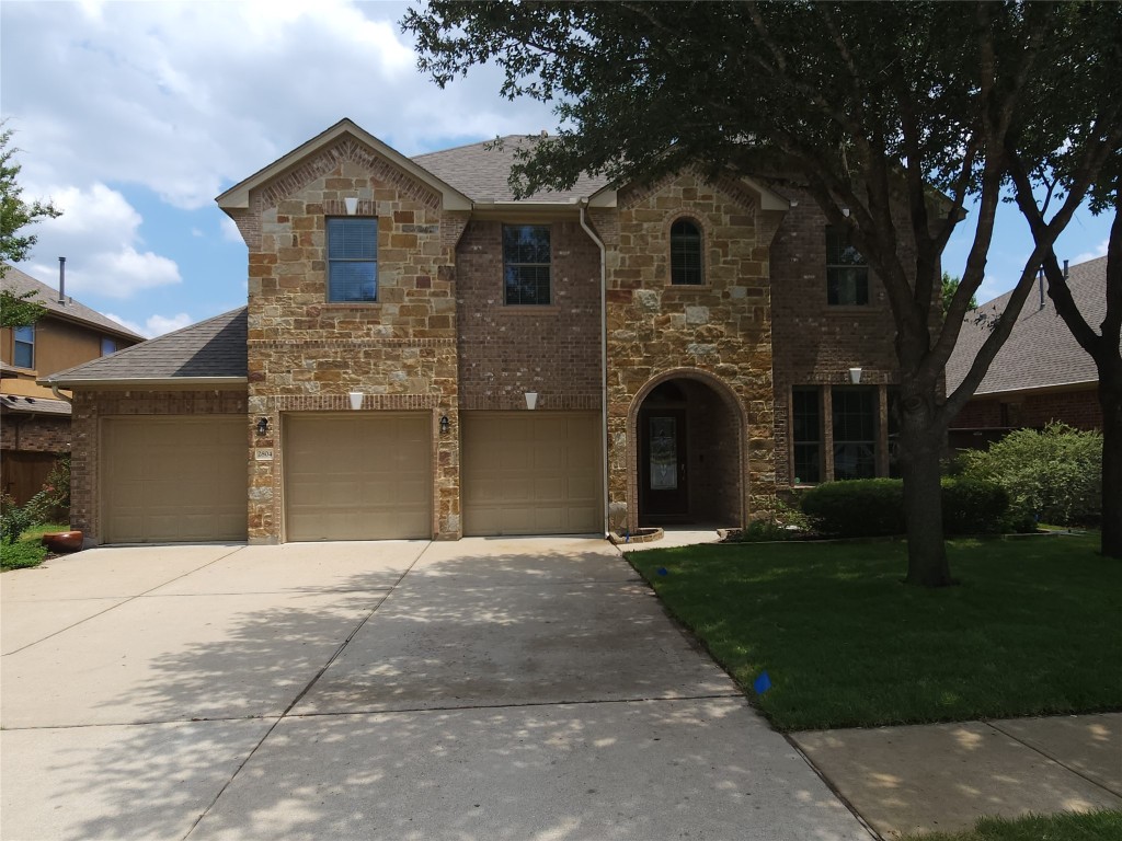 View of front of home featuring stone siding, a shingled roof, a garage, driveway, and a front yard