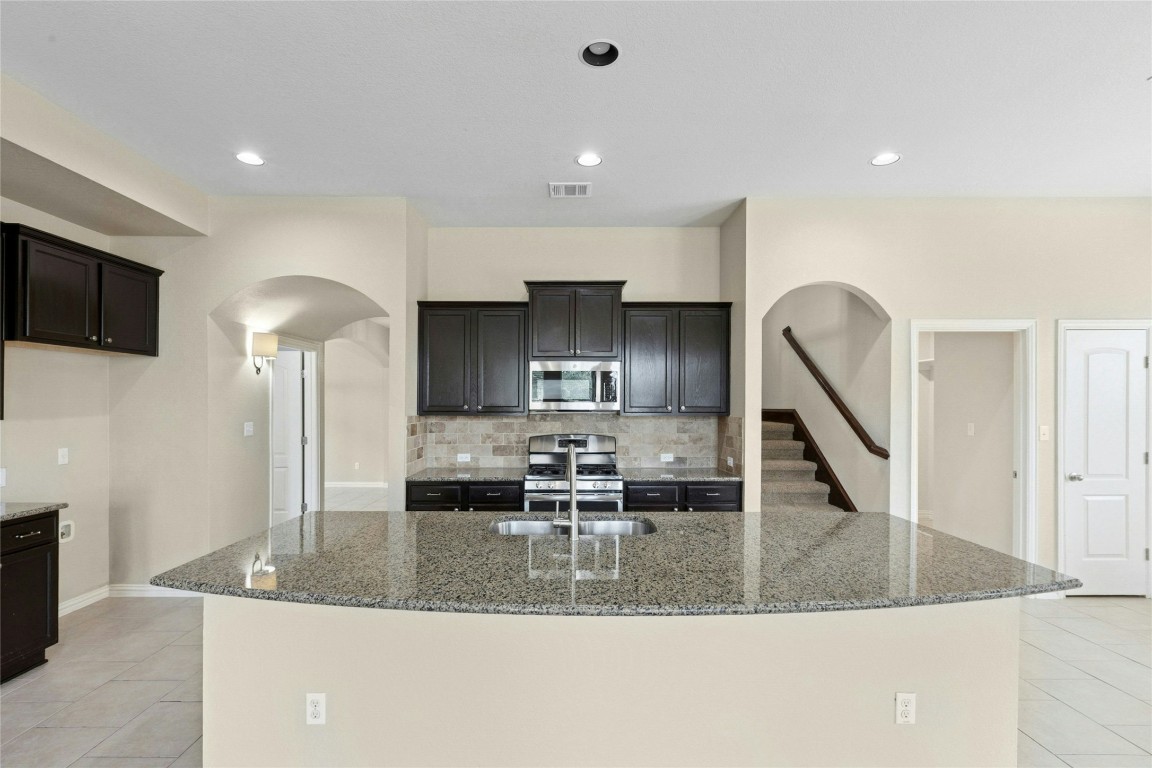 2804 Prosperity Leander, TX 78641 - Photo 8 of 39 Kitchen featuring stainless steel appliances, arched walkways, light tile patterned flooring, tasteful backsplash, and stone countertops