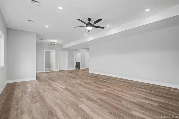 a view of an empty room with wooden floor and a ceiling fan