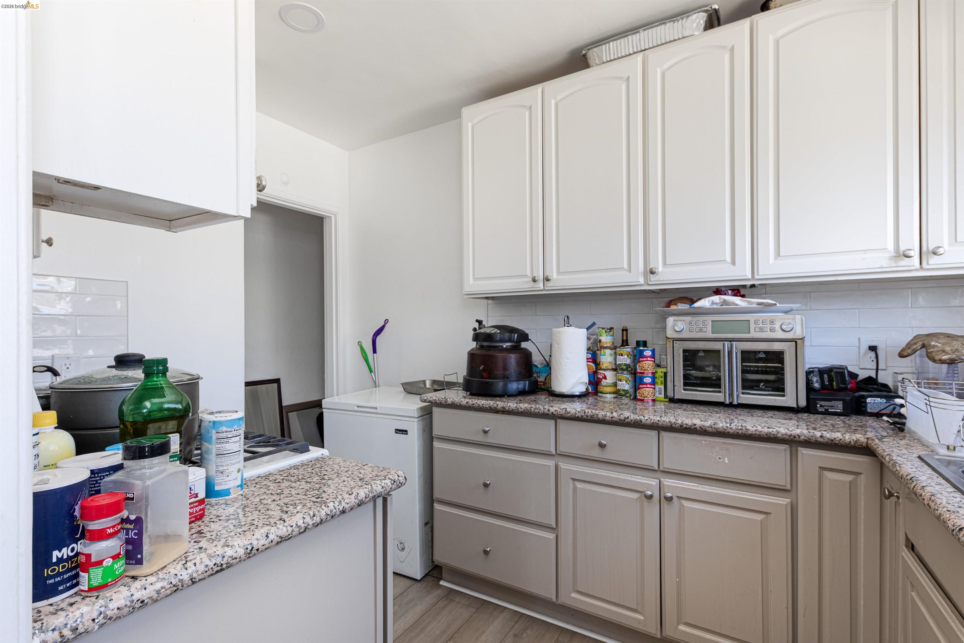 1821 74th Avenue Oakland, CA 94621 - Photo 21 of 27 Kitchen with tasteful backsplash, light stone countertops, white cabinets, and light wood finished floors