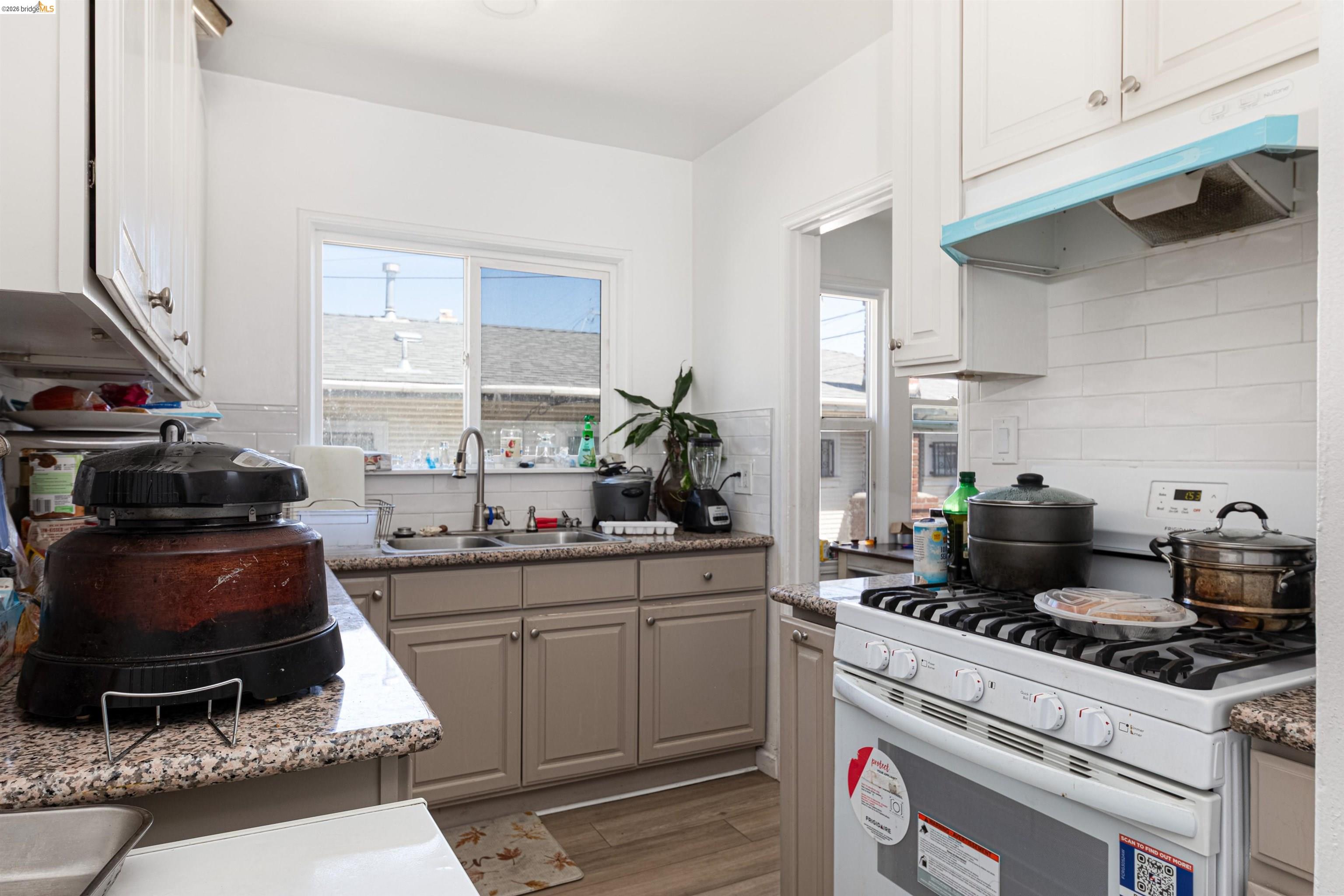 1821 74th Avenue Oakland, CA 94621 - Photo 22 of 27 Kitchen with white gas range, backsplash, under cabinet range hood, and healthy amount of natural light