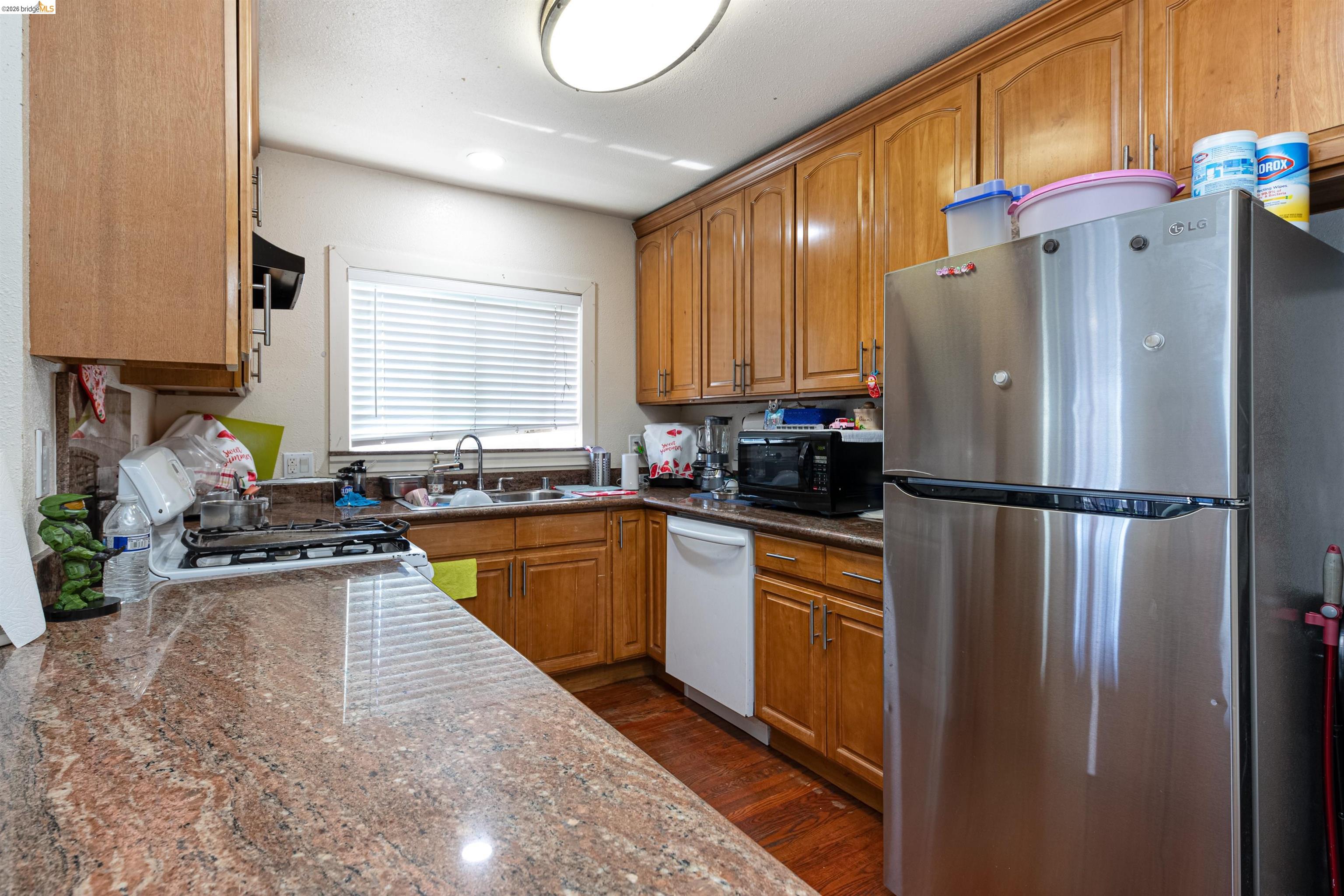 1821 74th Avenue Oakland, CA 94621 - Photo 7 of 27 Kitchen with white appliances, brown cabinets, dark stone counters, and dark wood-type flooring