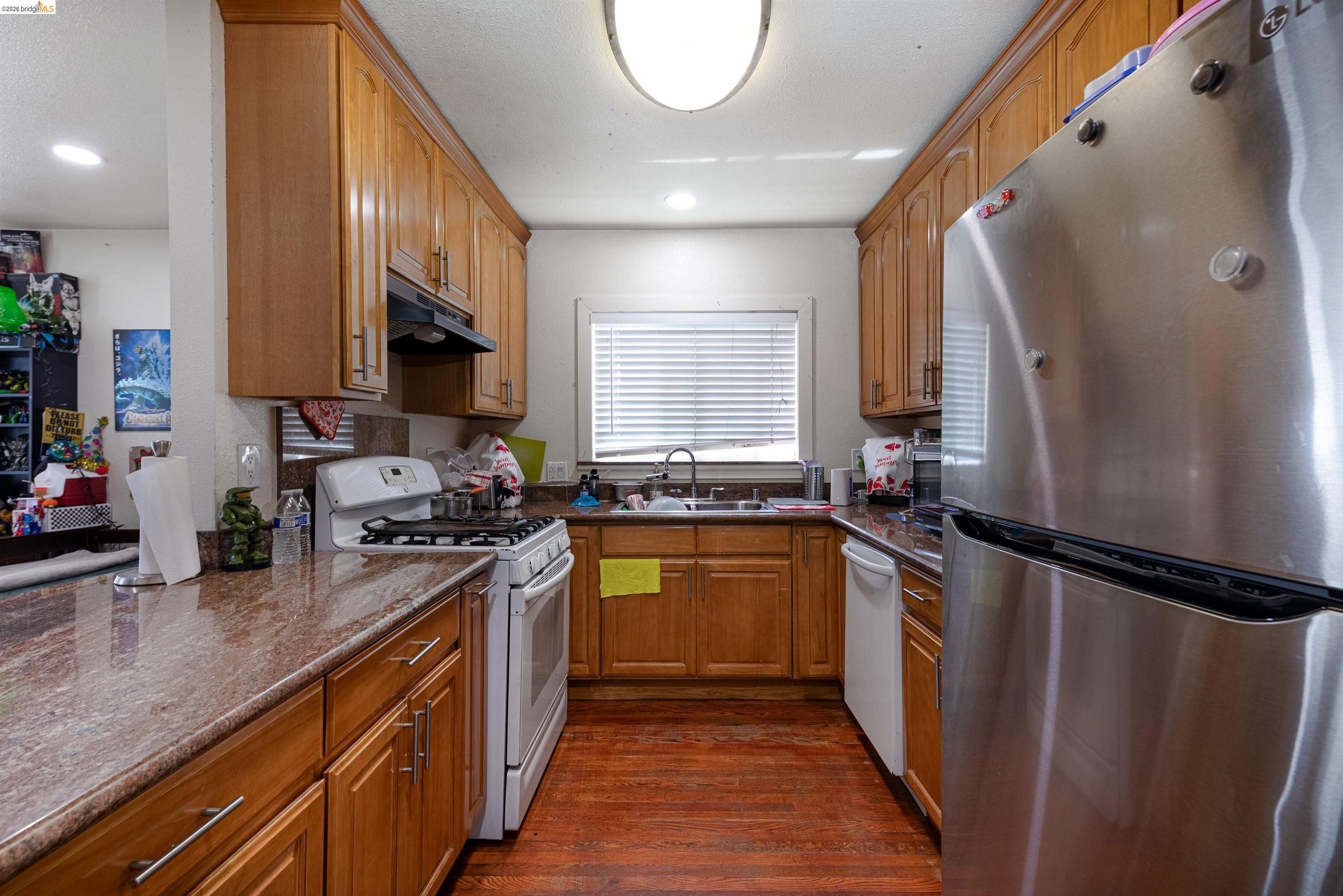 1821 74th Avenue Oakland, CA 94621 - Photo 8 of 27 Kitchen with white appliances, brown cabinets, dark wood-style flooring, dark stone counters, and under cabinet range hood