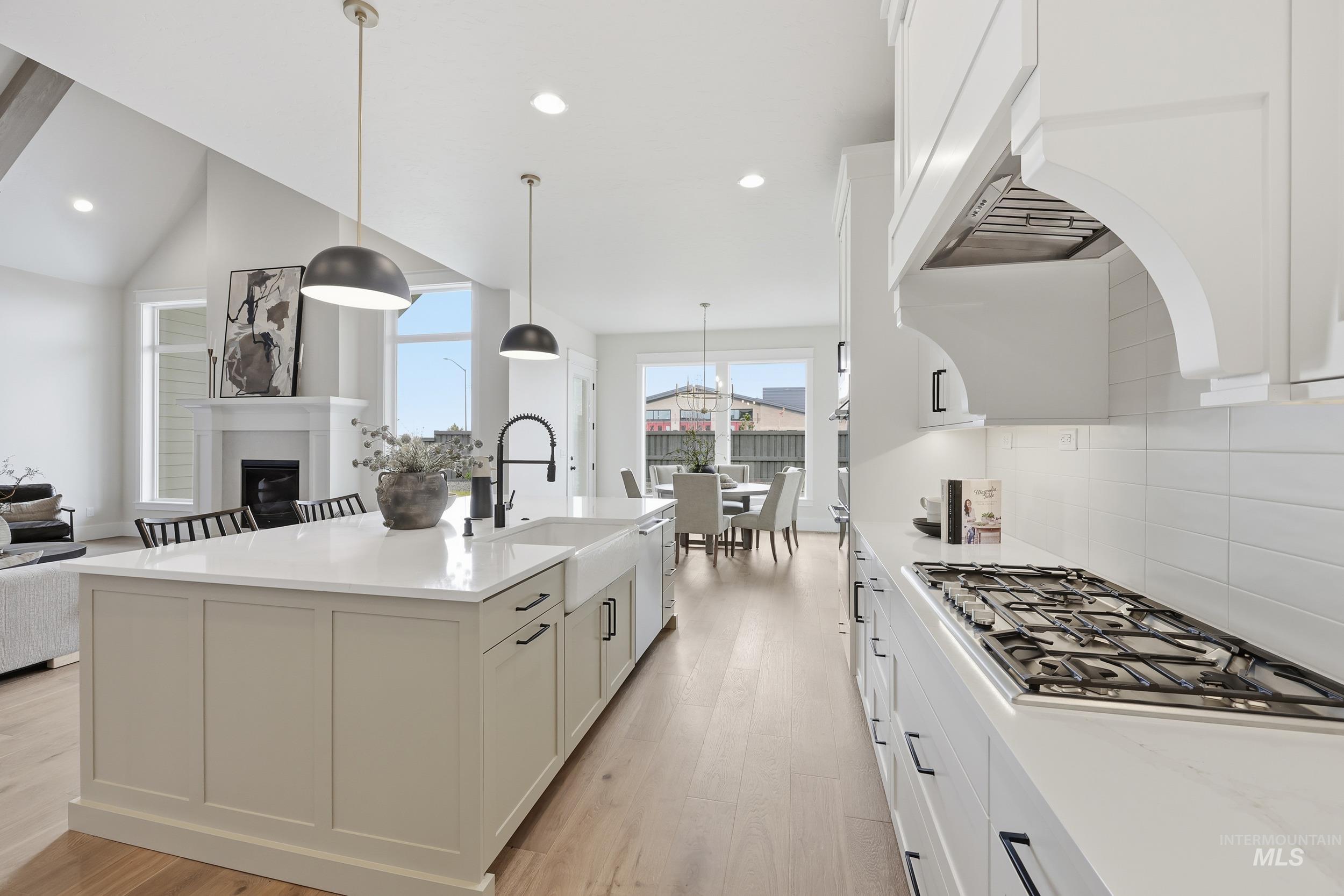 6513 South Utmost Way Meridian, ID 83642 - Photo 14 of 47 Kitchen with white cabinets, tasteful backsplash, a fireplace, light wood-style flooring, and decorative light fixtures