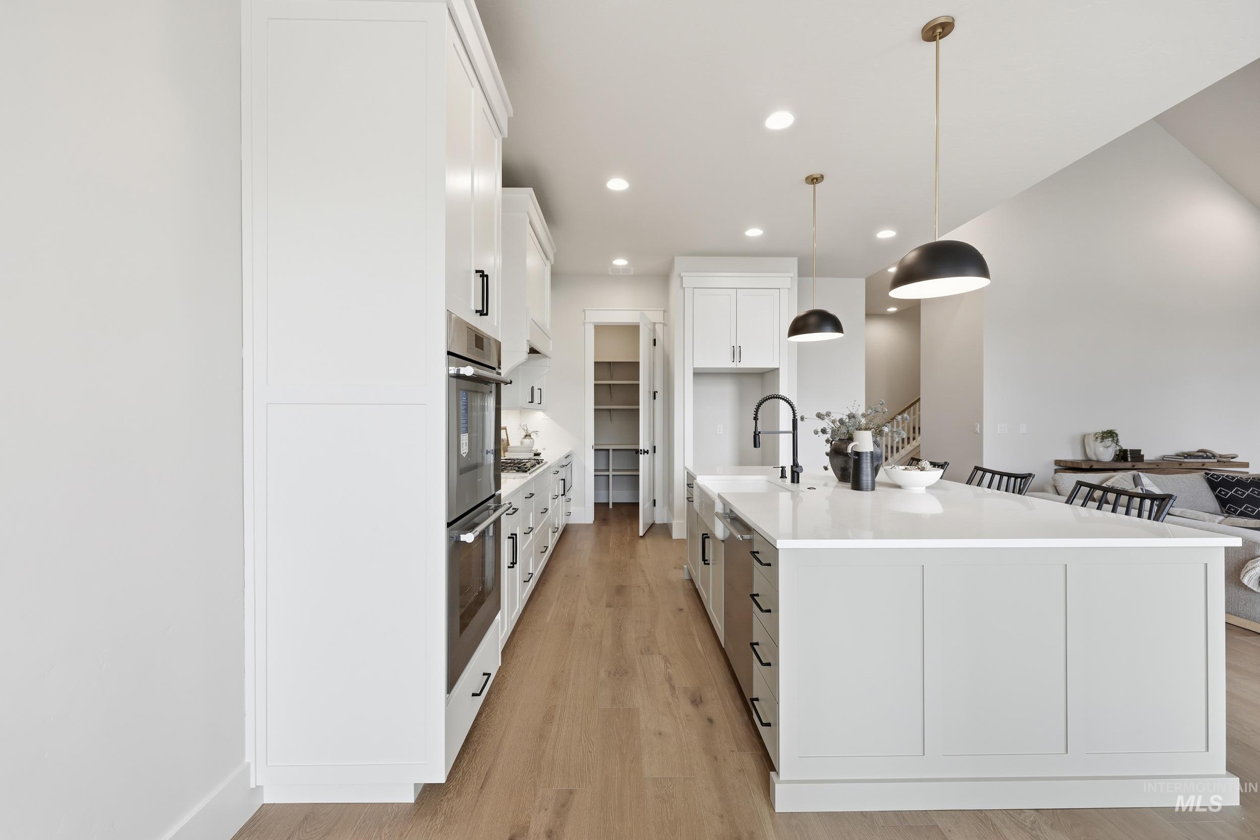 6513 South Utmost Way Meridian, ID 83642 - Photo 16 of 47 Kitchen featuring white cabinets, recessed lighting, light wood finished floors, hanging light fixtures, and a kitchen island with sink