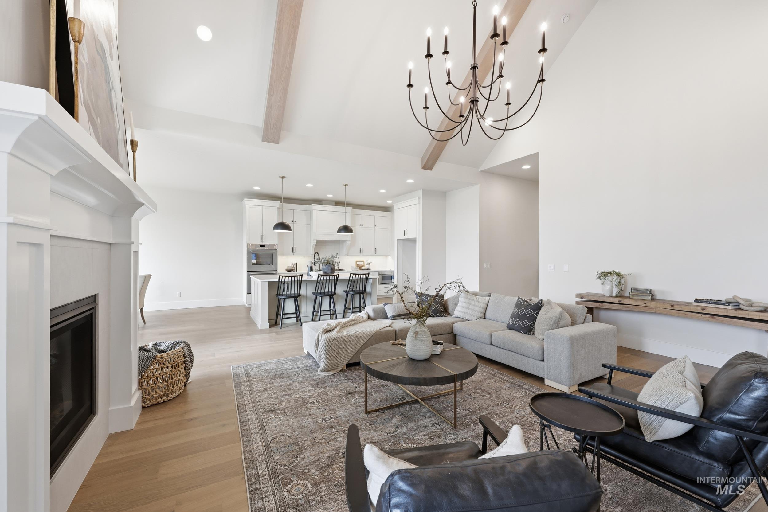 6513 South Utmost Way Meridian, ID 83642 - Photo 4 of 47 Living room featuring beamed ceiling, a glass covered fireplace, light wood-type flooring, a high ceiling, and a chandelier