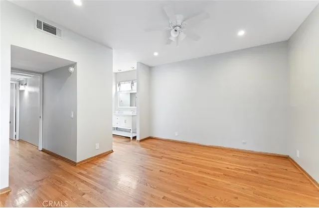a view of an empty room with wooden floor and a kitchen