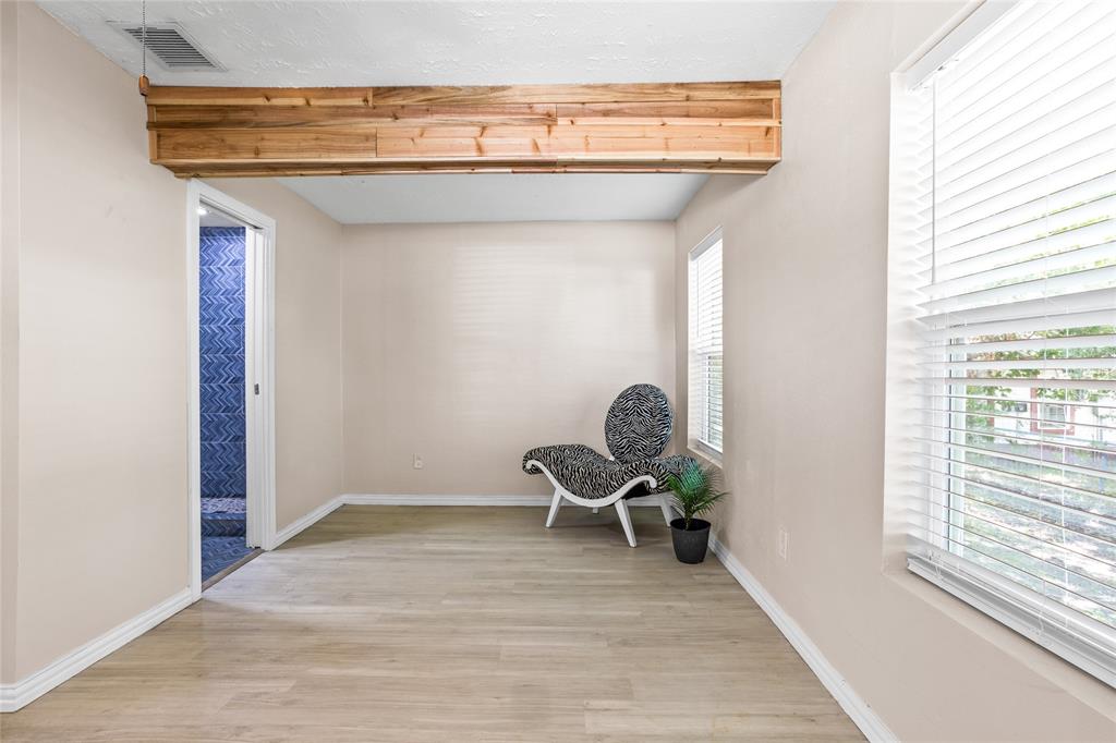 614 Rice Street Denison, TX 75020 - Photo 13 of 22 The primary bedroom has a lovely cedar beam for a fun accent. Three large windows bring in the light. On the left, there is a nice bathroom.