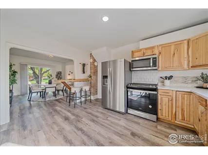 a kitchen with stainless steel appliances granite countertop a refrigerator a stove top oven a dining table and chairs with wooden floor