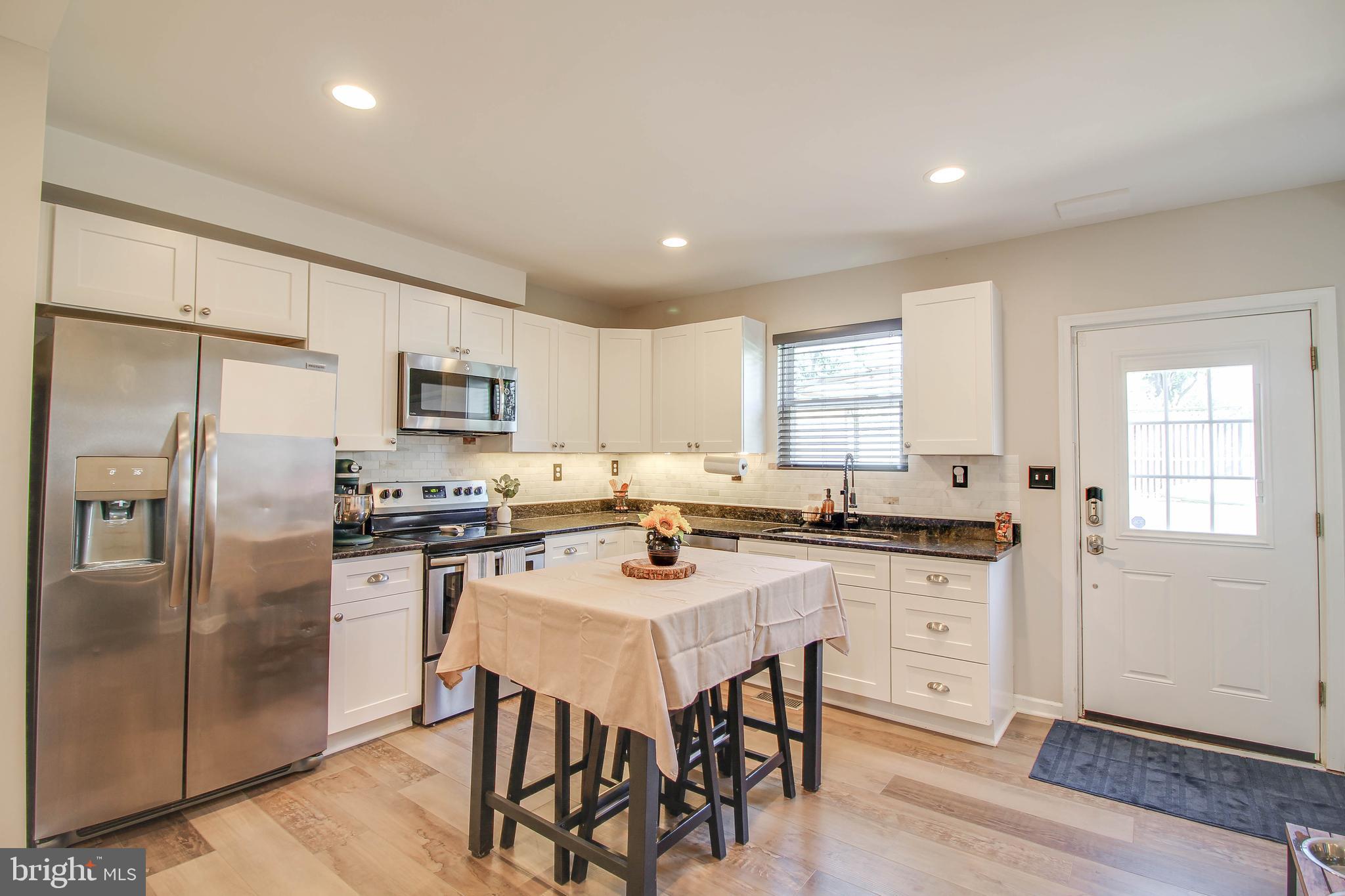 7805 Outing Avenue Pasadena, MD 21122 - Photo 10 of 51 a kitchen with stainless steel appliances granite countertop a stove a sink a refrigerator white cabinets and wooden floor