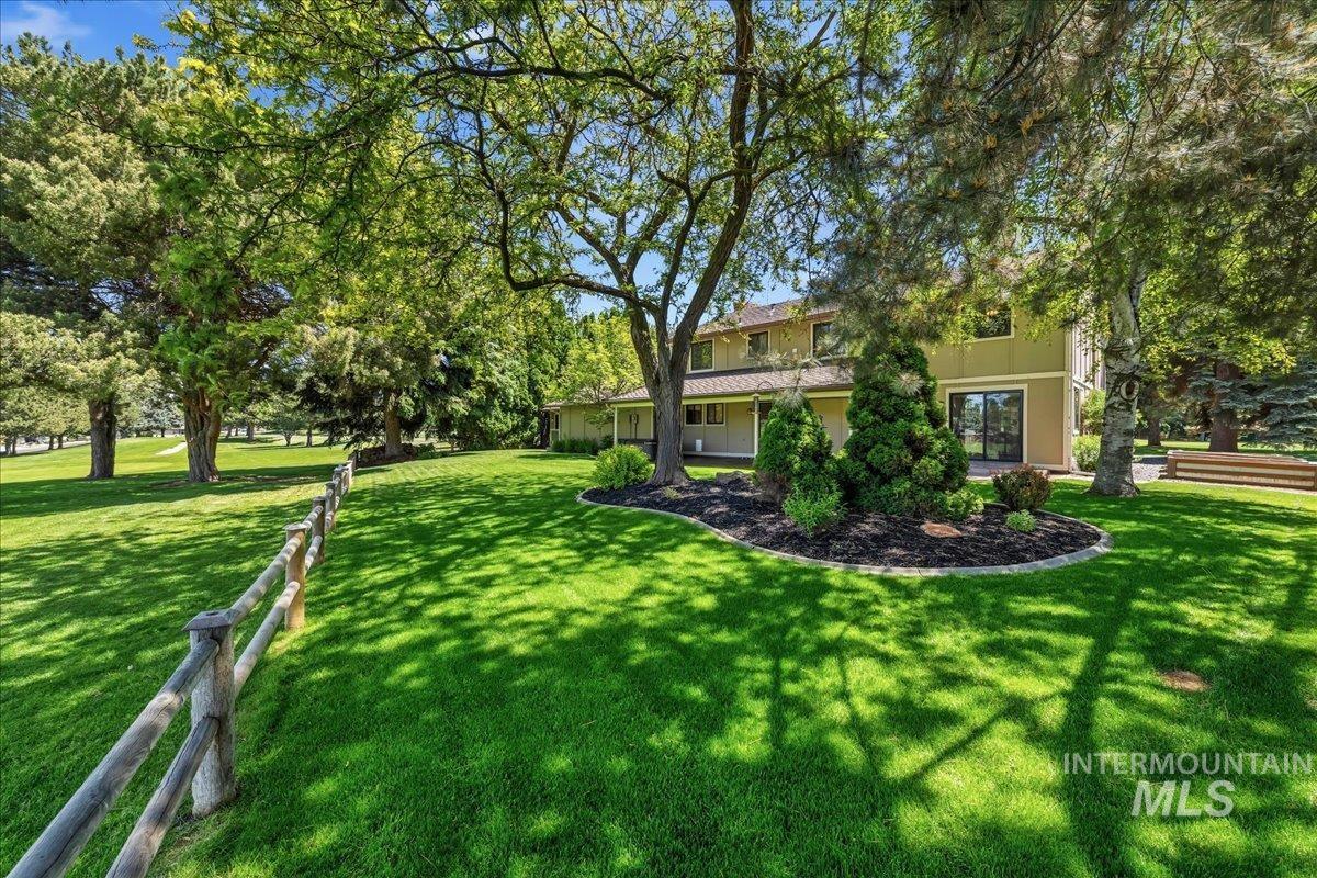599 Pebble Beach Way Eagle, ID 83616 - Photo 33 of 44 Spacious green lawn with a split-rail fence, mature shade trees, and a landscaped garden bed