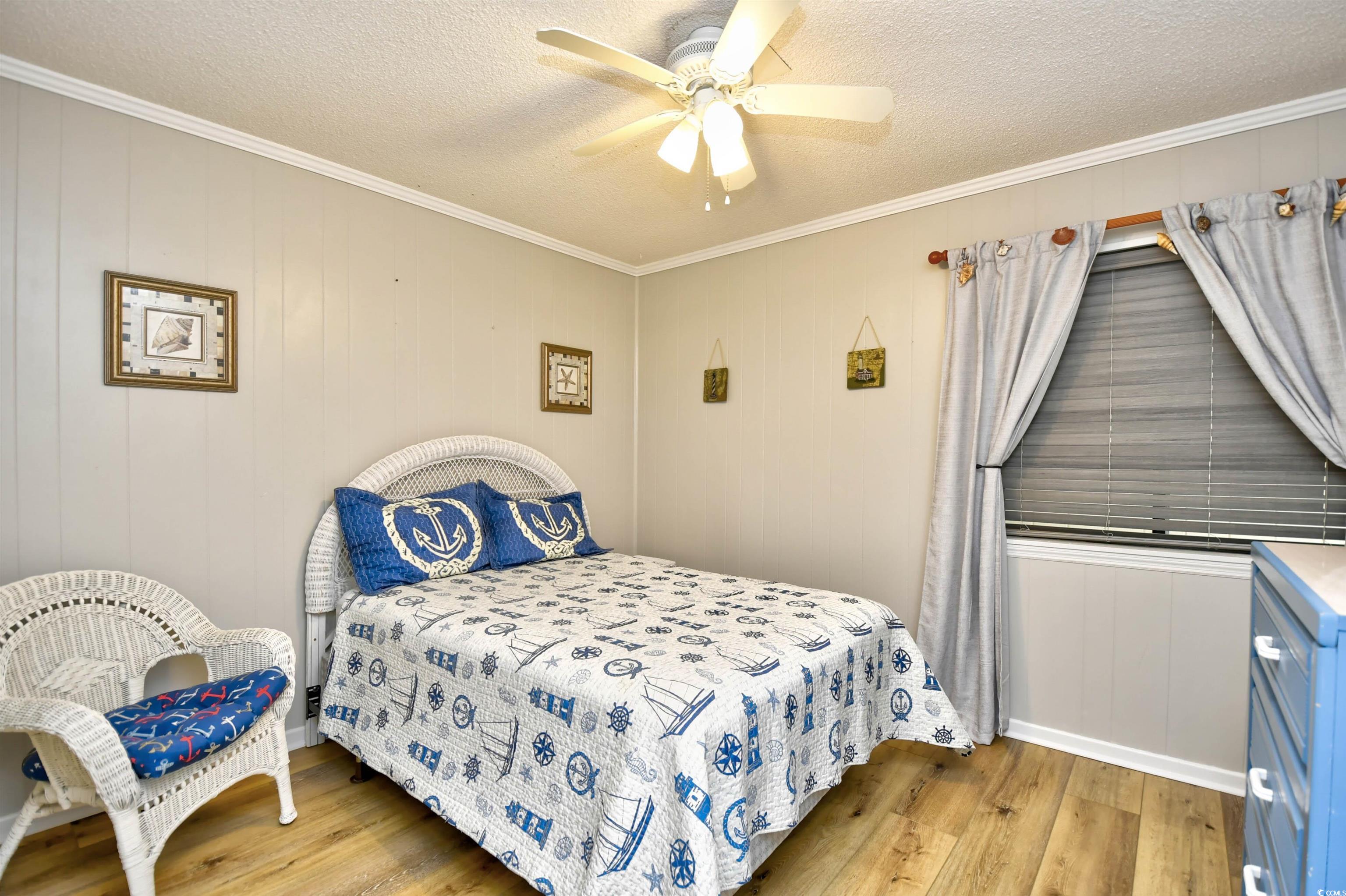 191 Maison Drive, Unit B211 Myrtle Beach, SC 29572 - Photo 17 of 35 Bedroom with light wood-type flooring, a ceiling fan, wooden walls, crown molding, and a textured ceiling