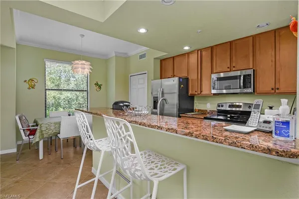 a kitchen with stainless steel appliances granite countertop a stove a sink a microwave a refrigerator and chairs