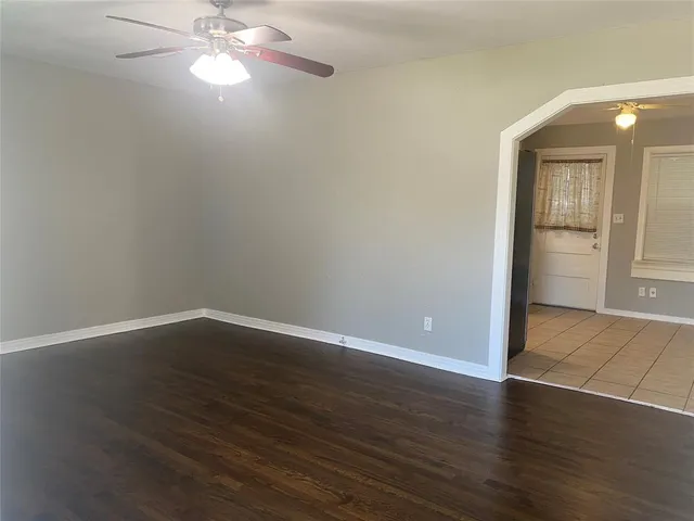 a view of an empty room with wooden floor and a ceiling fan