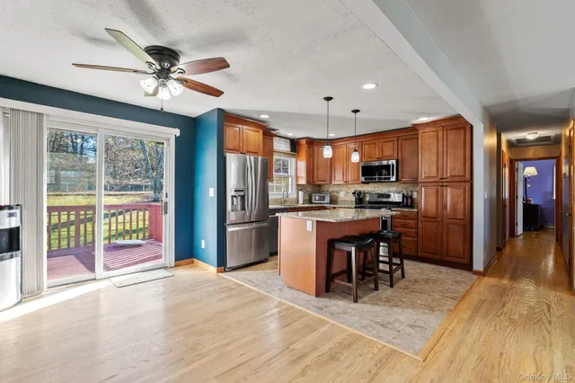 a kitchen with stainless steel appliances kitchen island granite countertop a refrigerator oven a sink a dining table and chairs with wooden floor