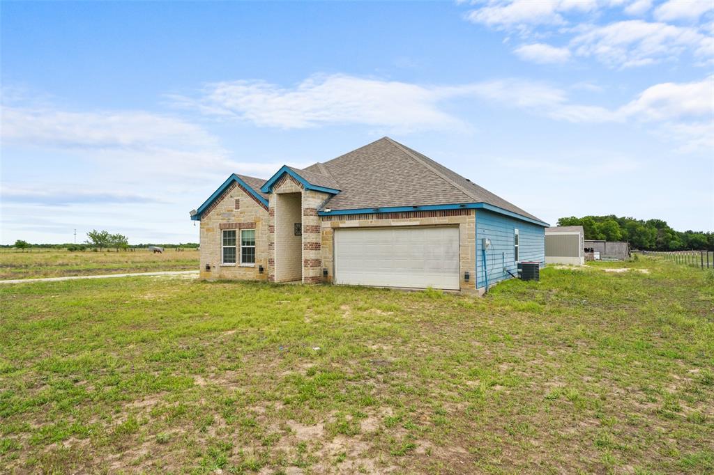 0 Ewing Road Ferris, TX 75125 - Photo 2 of 29 Exterior featuring a stone facade and light blue siding, a multi-pitched roofline, an attached garage, and a spacious grassy yard