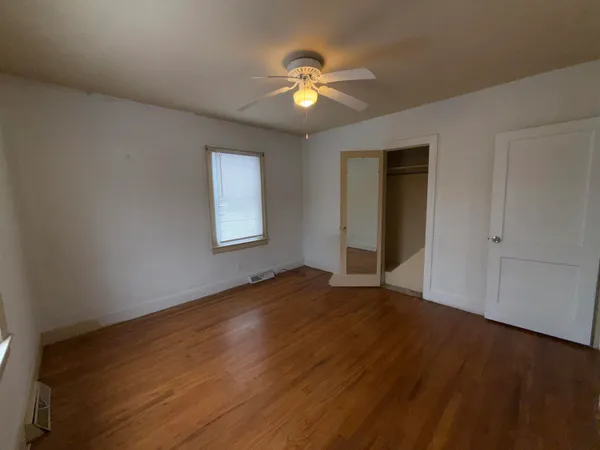 a view of an empty room with wooden floor and a ceiling fan