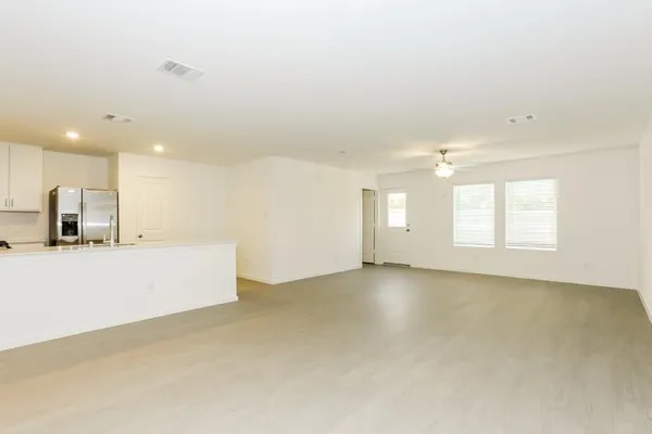 an empty room with windows and view of kitchen
