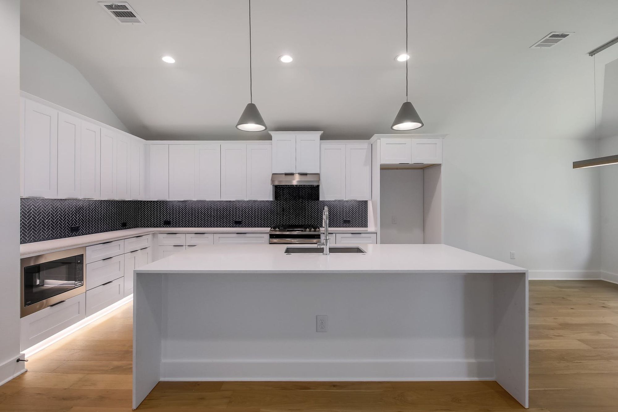 8302 Kromer Street Austin, TX 78757 - Photo 15 of 34 Kitchen featuring white cabinetry, light stone countertops, light wood-style flooring, an island with sink, and vaulted ceiling