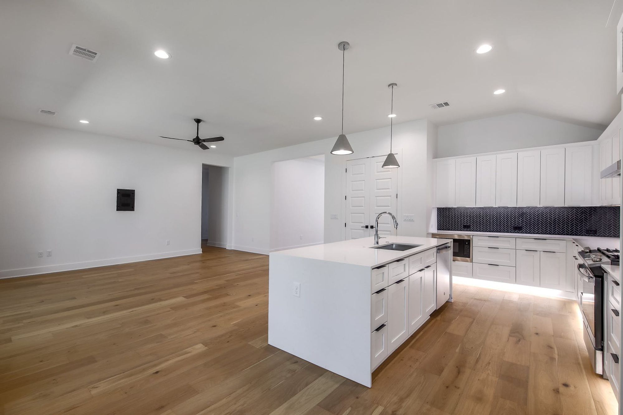 8302 Kromer Street Austin, TX 78757 - Photo 20 of 34 Kitchen with backsplash, an island with sink, white cabinetry, and decorative light fixtures