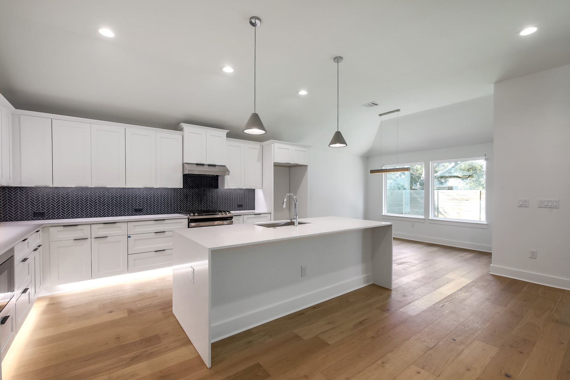 8302 Kromer Street Austin, TX 78757 - Photo 22 of 34 Kitchen with decorative backsplash, white cabinets, vaulted ceiling, an island with sink, and stainless steel gas stove