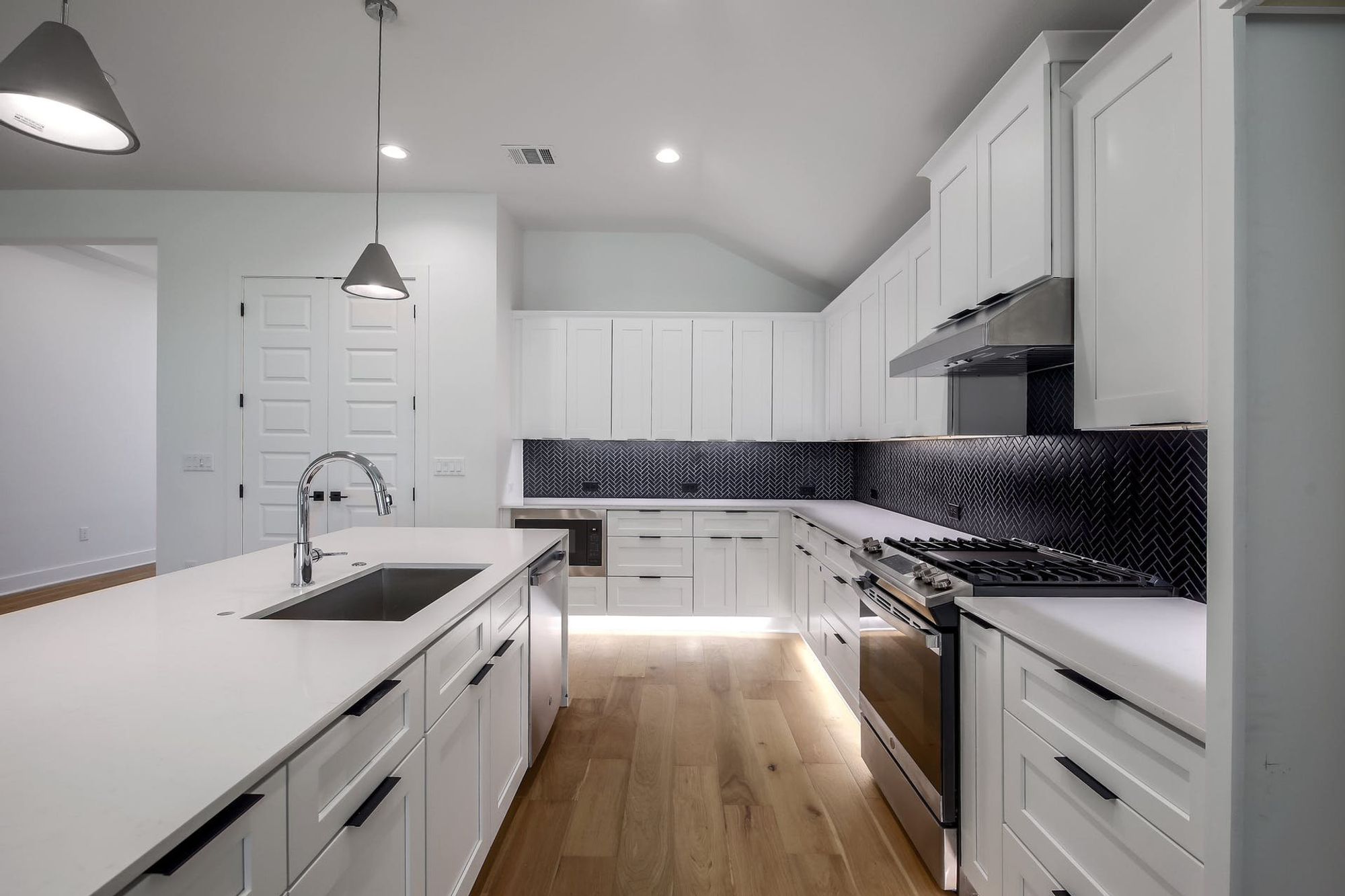 8302 Kromer Street Austin, TX 78757 - Photo 27 of 34 Kitchen with decorative backsplash, stainless steel appliances, white cabinetry, light wood-style flooring, and decorative light fixtures