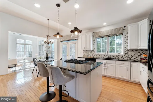 a kitchen with stainless steel appliances granite countertop a stove a refrigerator a kitchen island a dining table and chairs with wooden floor