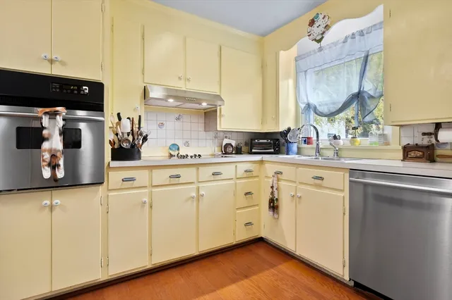a kitchen with stainless steel appliances granite countertop a sink a stove and white cabinets with wooden floor