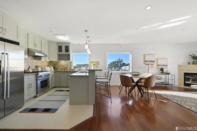 a kitchen with stainless steel appliances granite countertop a refrigerator a sink a stove a dining table and chairs