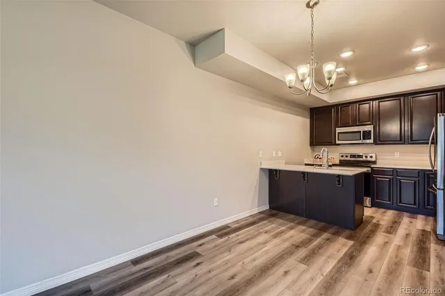 a kitchen with stainless steel appliances granite countertop a refrigerator a sink dishwasher a stove and a dining table with wooden floor