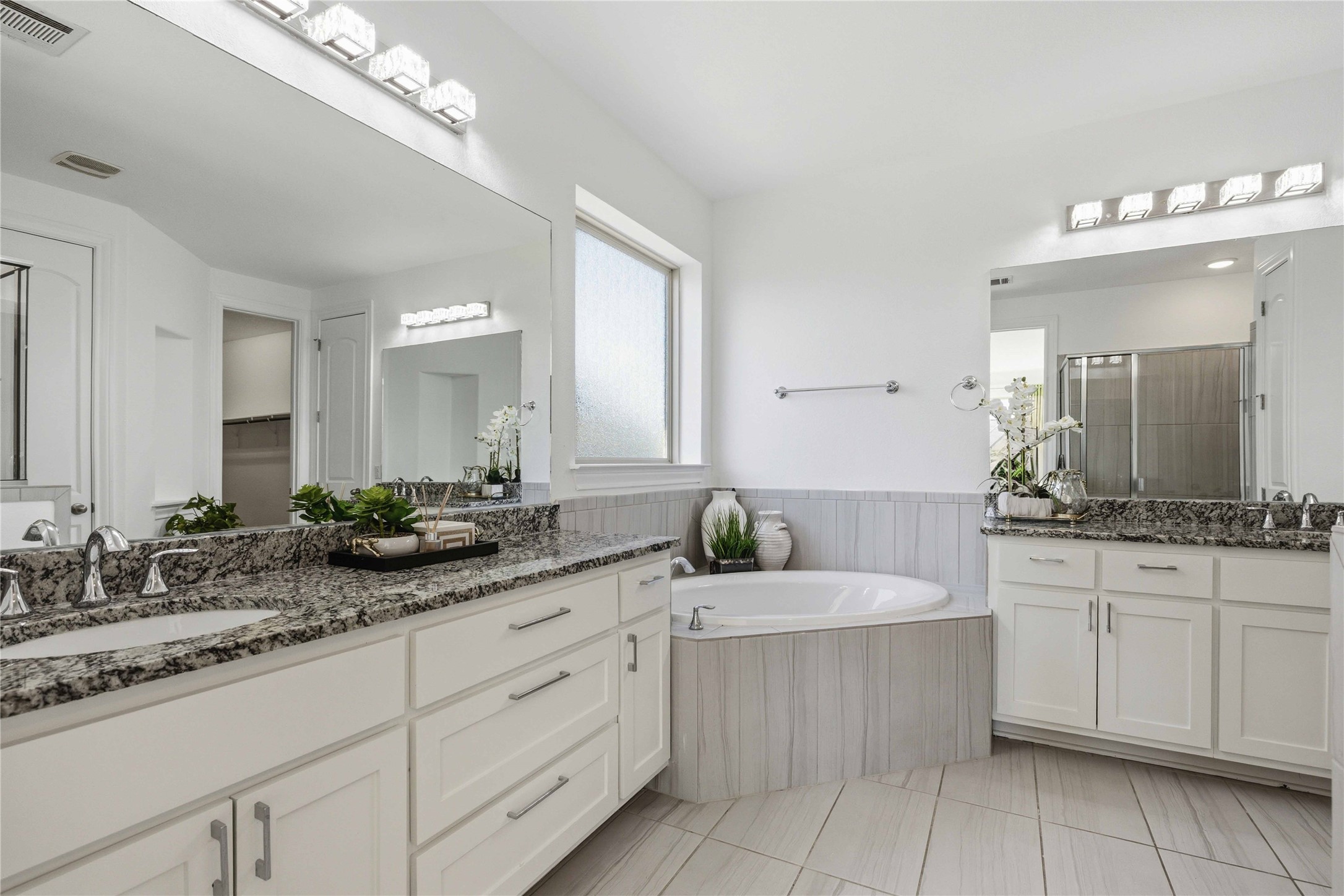 1517 Bardella Drive Leander, TX 78641 - Photo 13 of 40 Full bath featuring two vanities, a bath, a stall shower, light tile patterned flooring, and wainscoting