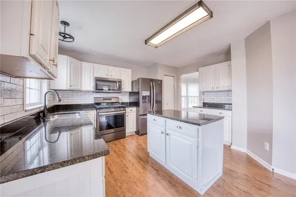 a kitchen with granite countertop a sink stainless steel appliances and white cabinets