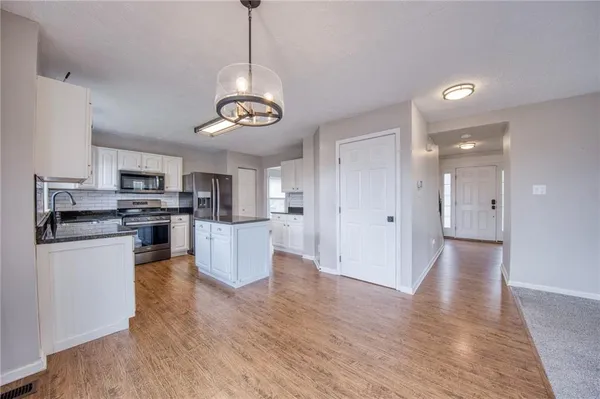 a view of kitchen with stainless steel appliances granite countertop wooden floors and white cabinets