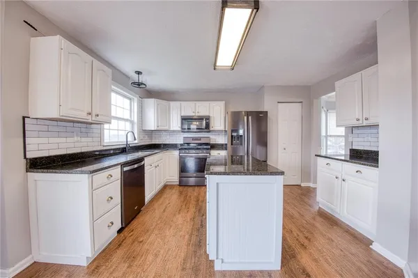 a kitchen with stainless steel appliances granite countertop a refrigerator a stove top oven a sink dishwasher and white cabinets with wooden floor