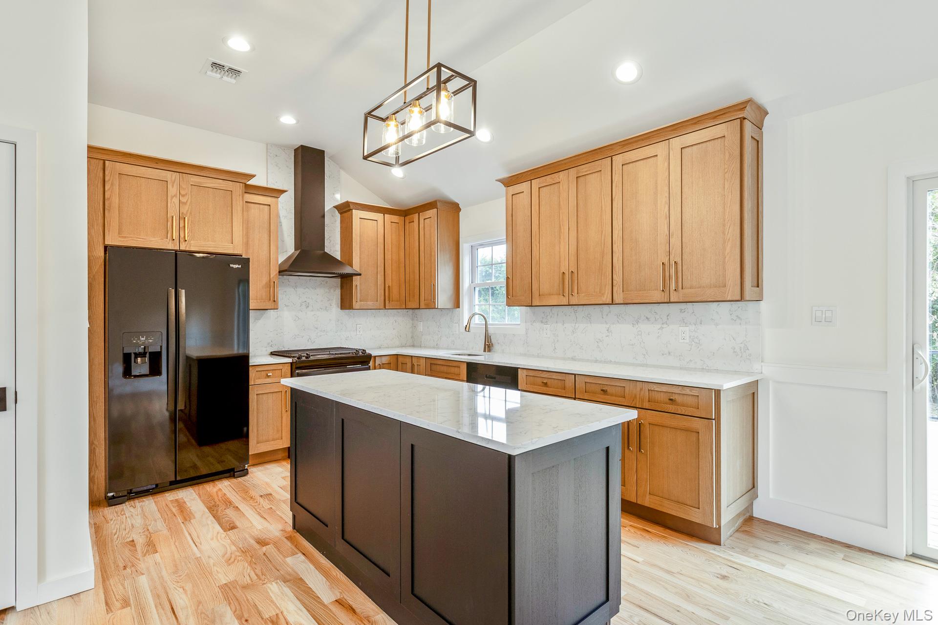 92 Park Street Blue Point, NY 11715 - Photo 22 of 32 Kitchen featuring black refrigerator with ice dispenser, light stone counters, tasteful backsplash, a center island, and wall chimney exhaust hood