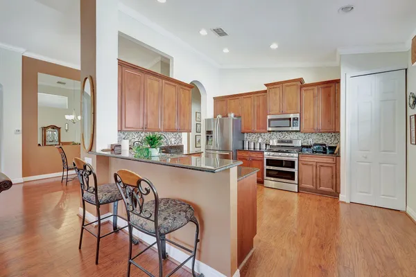 a kitchen with stainless steel appliances a stove a sink a refrigerator and a dining table with wooden floor