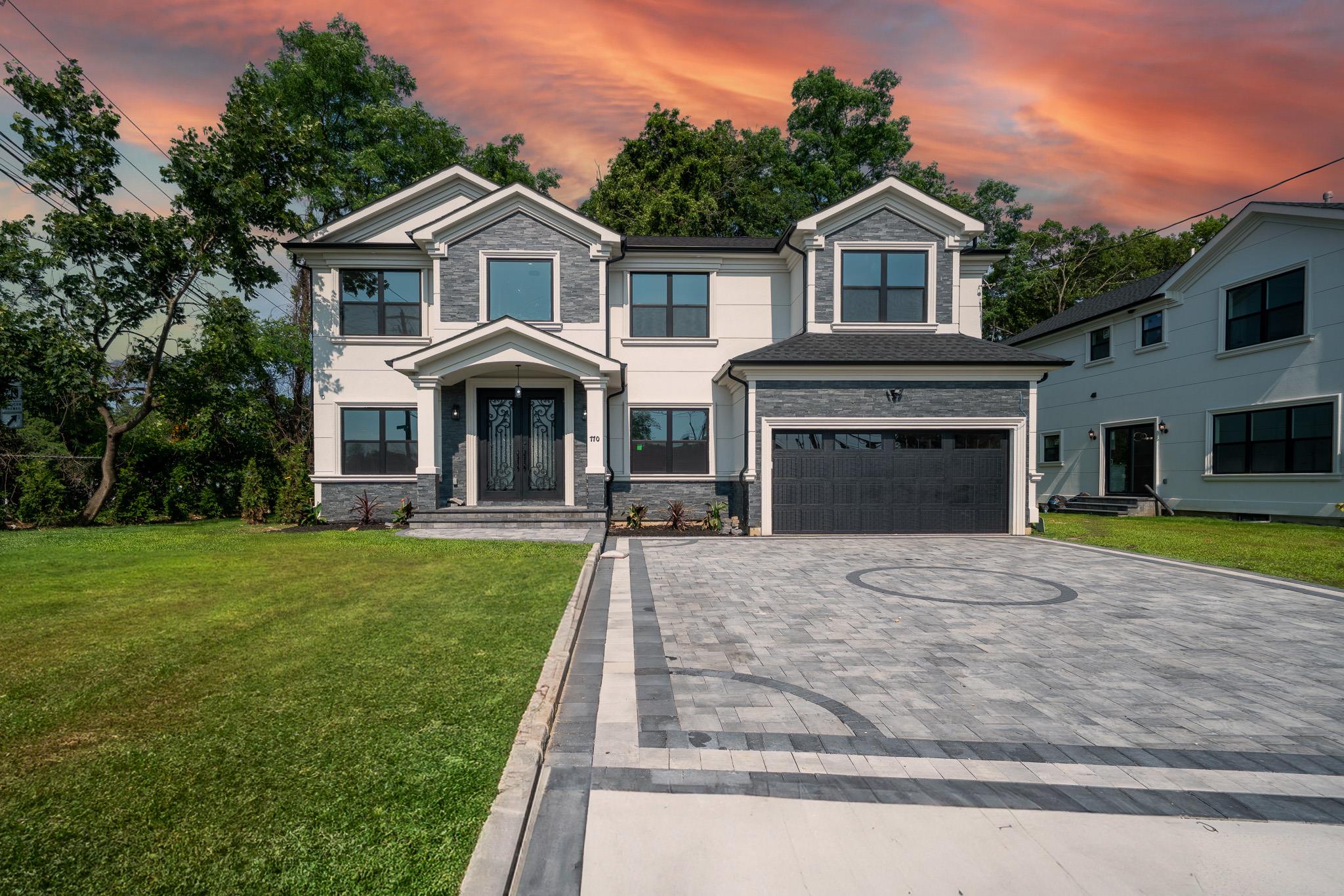 View of front facade featuring decorative driveway, an attached garage, stone siding, and a yard