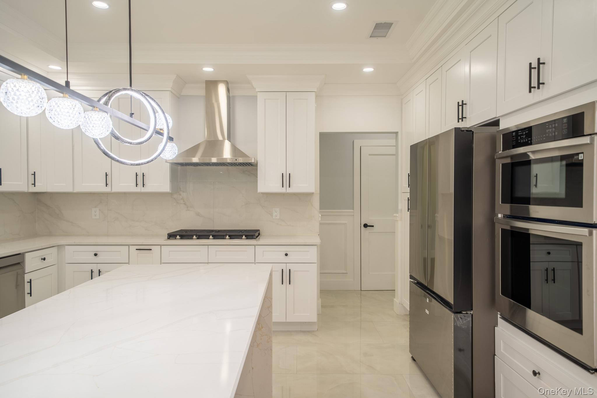 770 Cedar Street Syosset, NY 11791 - Photo 13 of 35 Kitchen featuring stainless steel appliances, decorative backsplash, crown molding, white cabinetry, and wall chimney exhaust hood