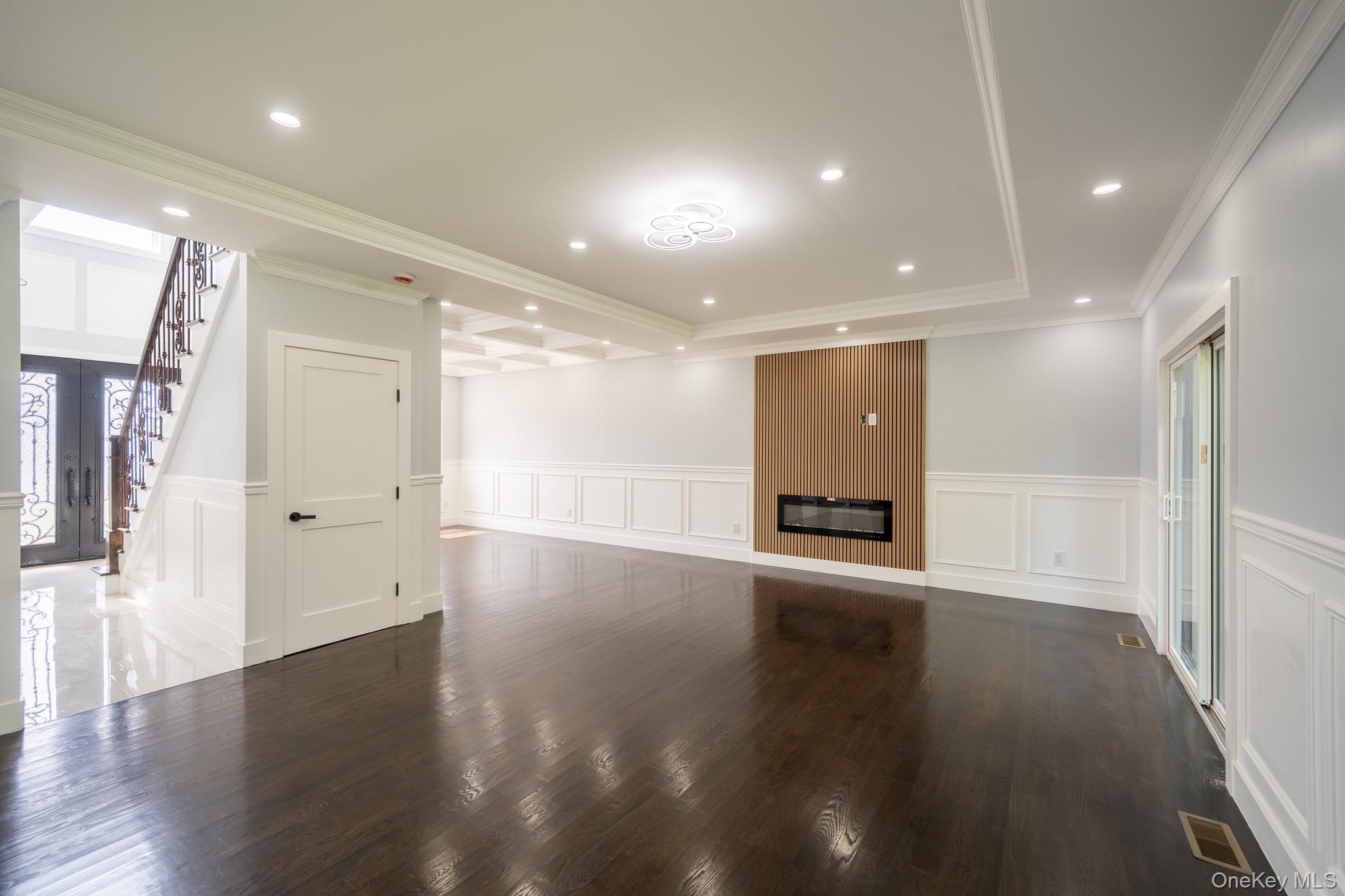 770 Cedar Street Syosset, NY 11791 - Photo 8 of 35 Unfurnished living room with wainscoting, a decorative wall, ornamental molding, dark wood-type flooring, and stairway