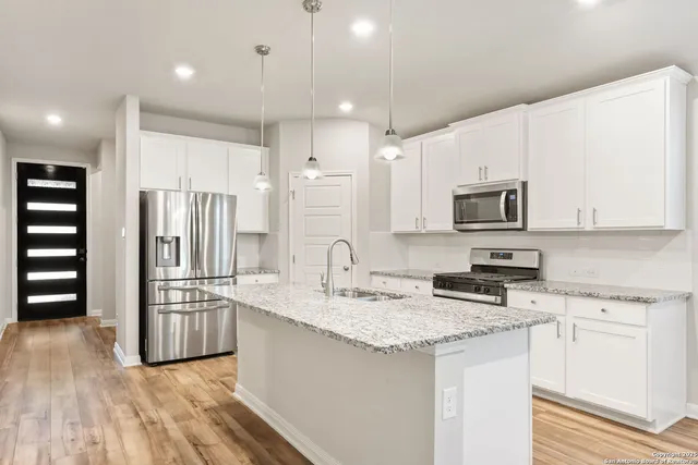 a kitchen with stainless steel appliances granite countertop a refrigerator a stove a sink and white cabinets with wooden floor