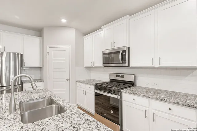 a kitchen with granite countertop a sink stainless steel appliances and white cabinets